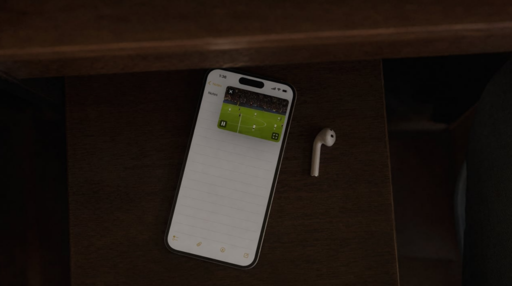 Phone with picture-in-picture soccer match floating over a notes app, tucked discreetly on a desk